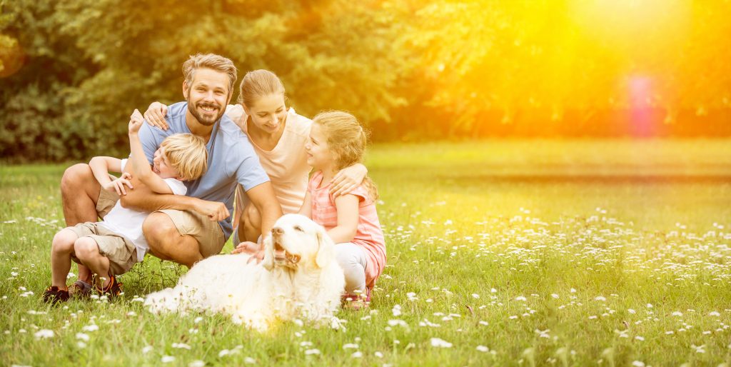 Glückliche Familie mit Kinder und Hund zusammen im Garten im Sommer