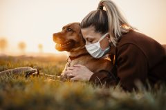 Woman wearing a protective mask is walking alone with a dog outdoors because of the corona virus pandemic covid-19